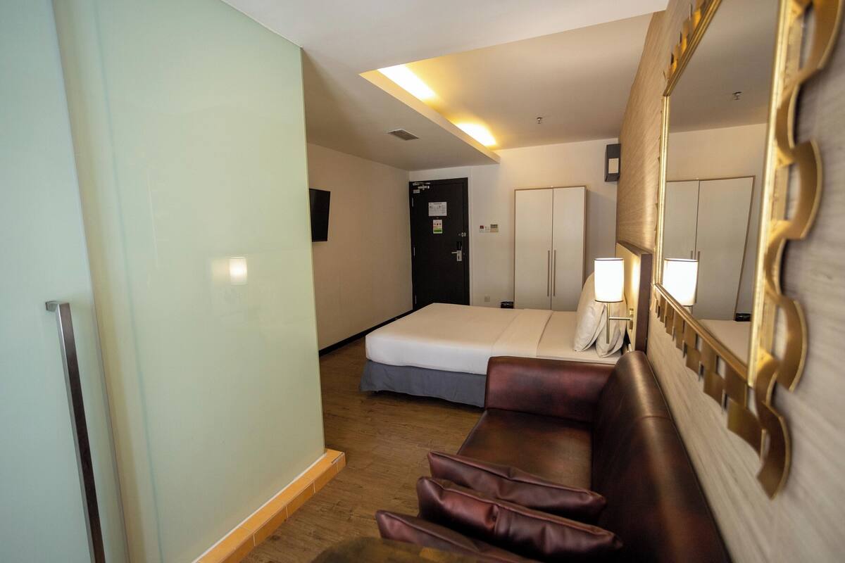 A hotel room with a bed, a sofa, a mirror, and a wardrobe.