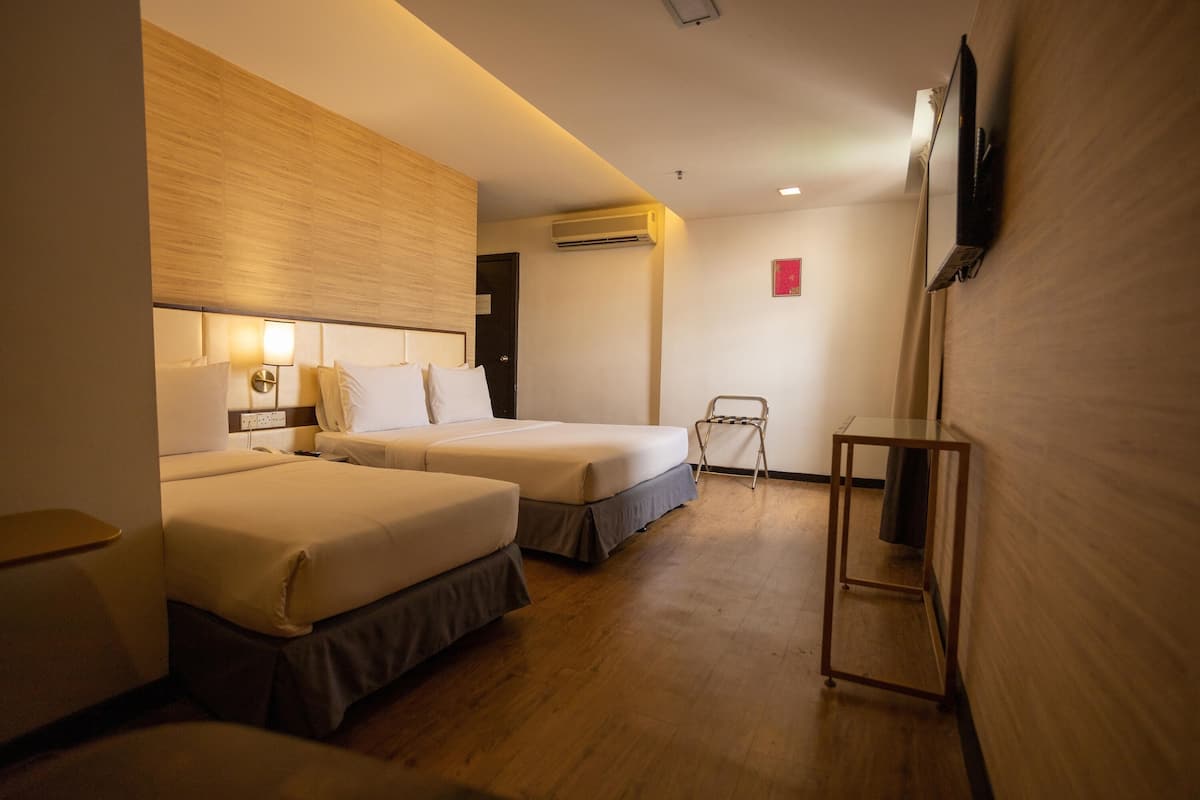 A hotel room with two beds, a TV mounted on the wall, an air conditioning unit, and a small table.