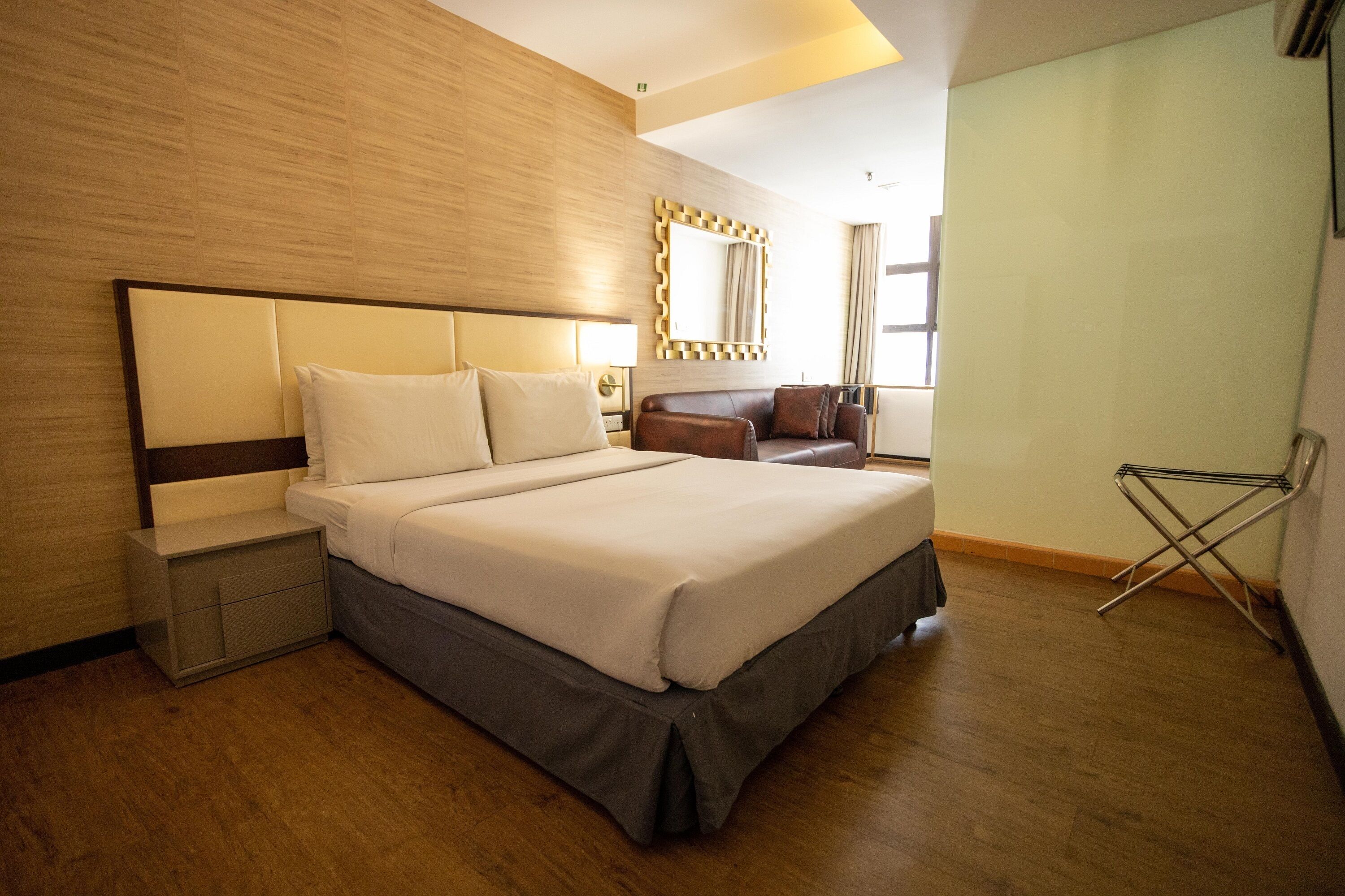 A modern hotel room with a large bed, a nightstand, a seating area with a sofa, and a window with curtains.