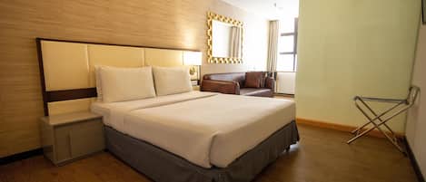 A modern hotel room with a large bed, a nightstand, a seating area with a sofa, and a window with curtains.