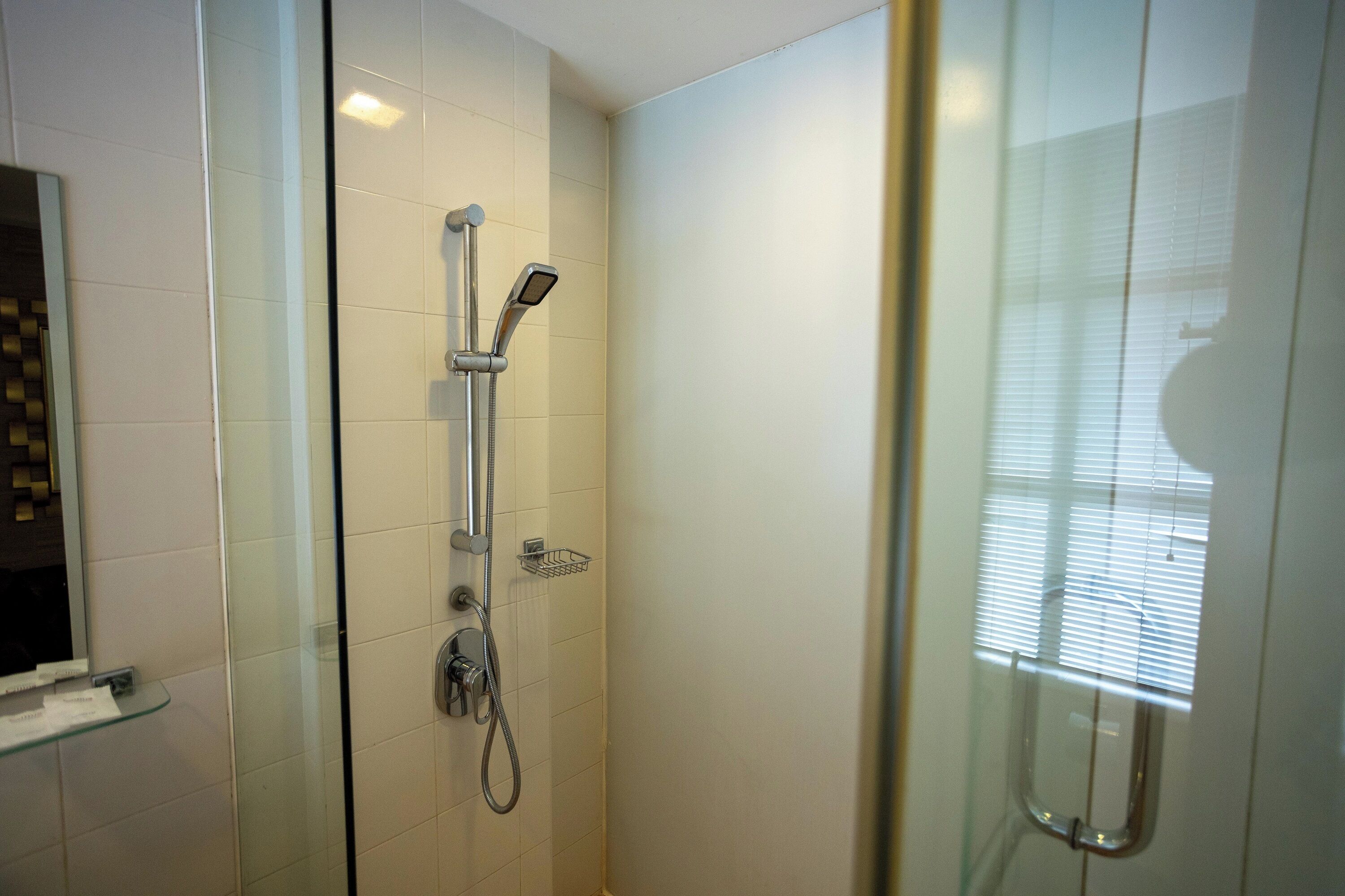 A glass-enclosed shower with a handheld showerhead and a wall-mounted faucet.