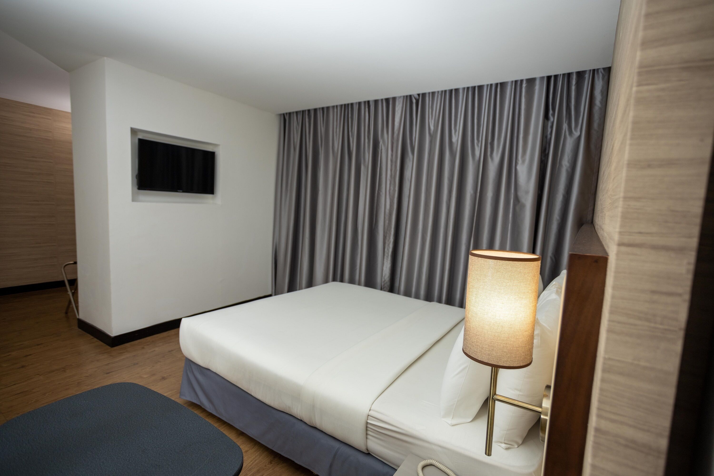 A hotel room with a bed, a bedside lamp, a window, and a curtain.