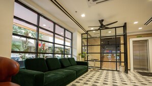 A reception area with a green sofa, a red chair, a patterned floor, a ceiling fan, and a view of the outside through large windows.