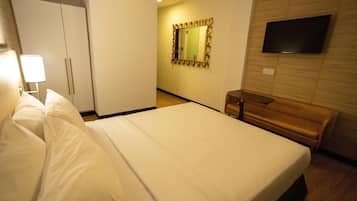 A hotel room with a bed, a wardrobe, a mirror, a television, and a bench.