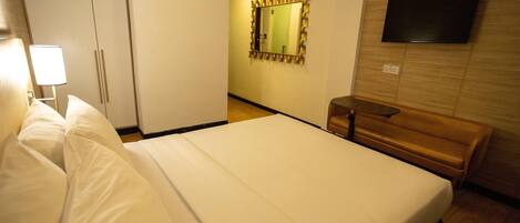 A hotel room with a bed, a wardrobe, a mirror, a television, and a bench.