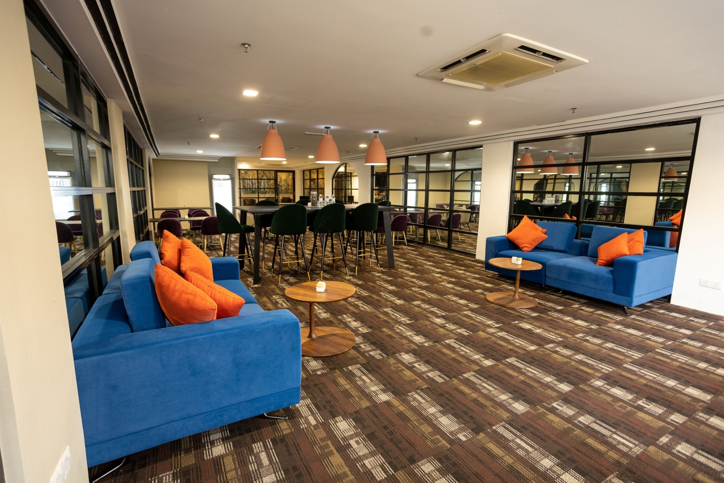 A spacious lobby with blue sofas, orange cushions, and a patterned carpet.