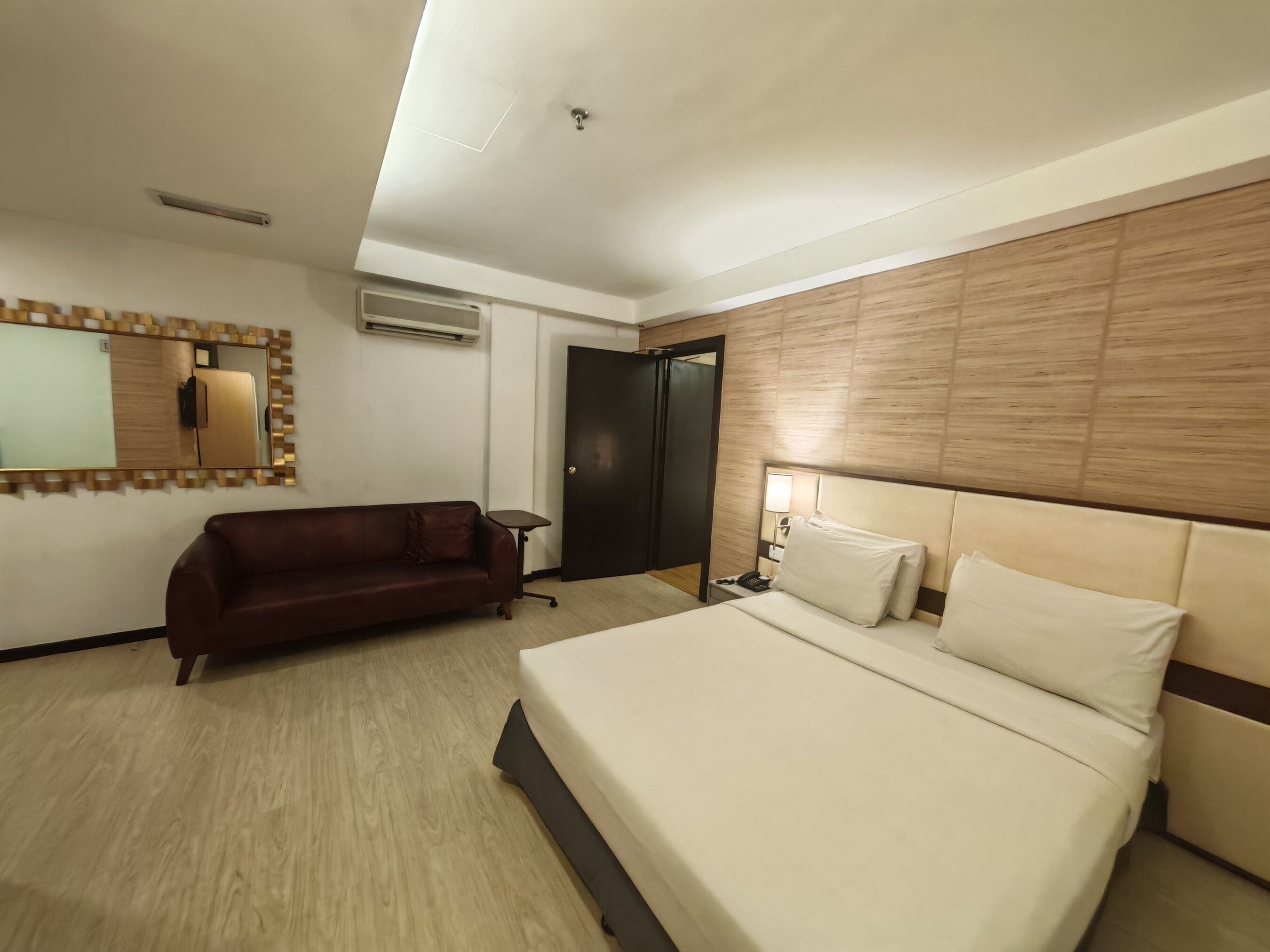 Habitación de hotel con cama, sofá, escritorio, espejo y puerta.