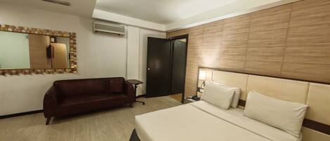 Habitación de hotel con cama, sofá, escritorio, espejo y puerta.