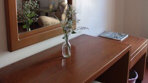 A wooden desk with a vase of flowers, a mirror, and a flat-screen TV mounted on the wall.