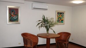 A room with a round wooden table, two leather chairs, and two framed abstract paintings on the walls.