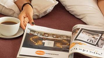 Una persona recostada en una cama con una revista abierta que muestra el interior de un hotel.