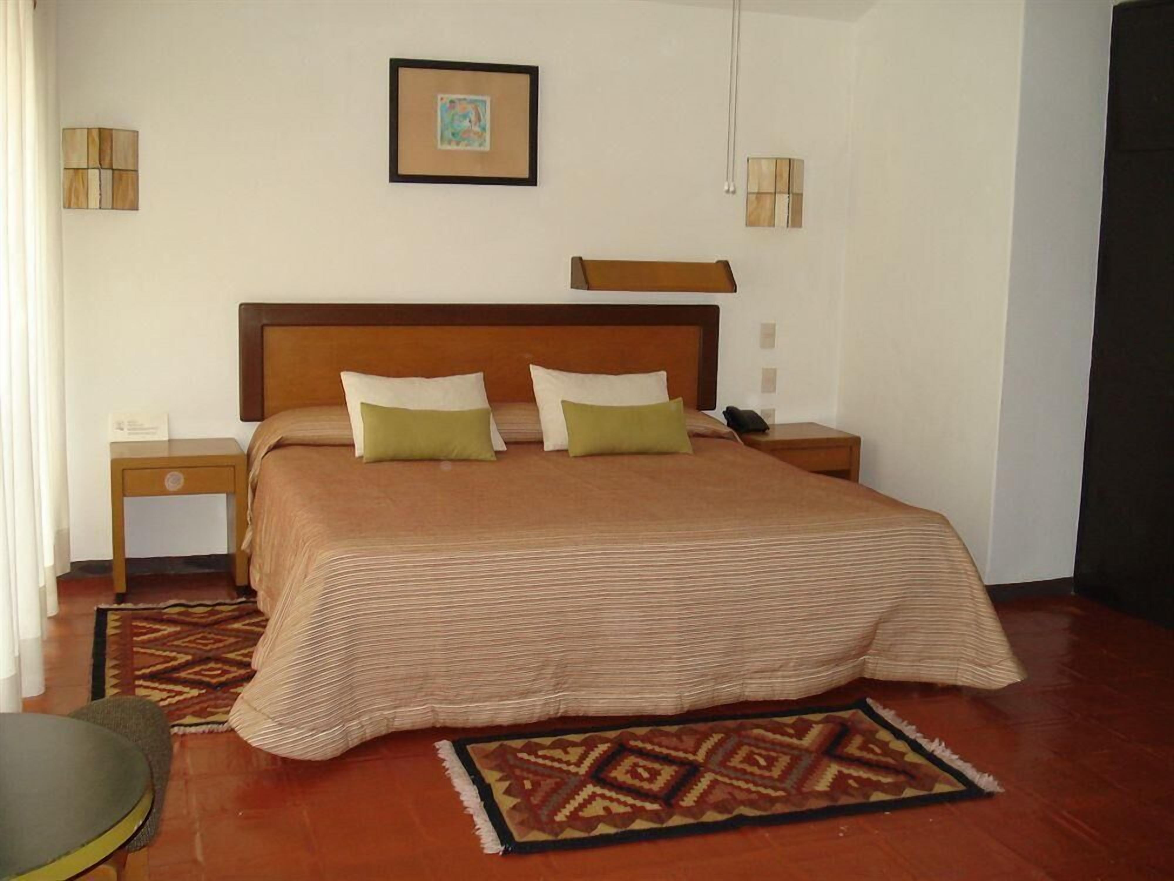 Een hotelkamer met een bed, nachtkastjes, een tapijt met patroon en een ingelijste foto aan de muur.
