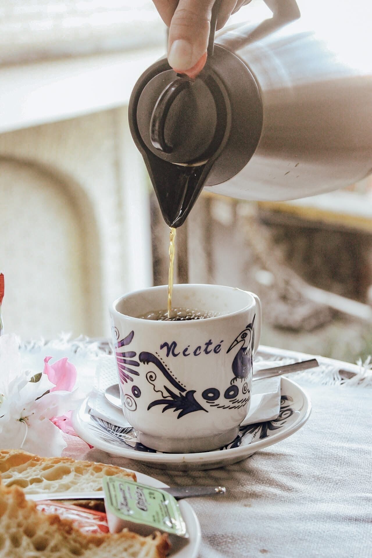 A hand pouring a dark liquid into a cup with a decorative design and the word "Nicté" on it.