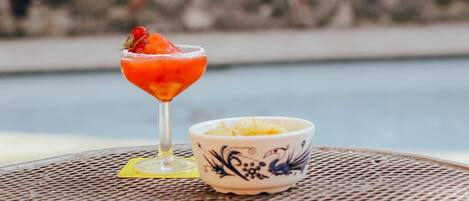 A cocktail glass with a strawberry garnish on a metal table next to a decorative bowl.