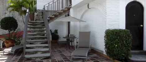 A courtyard with a stone staircase, a table with chairs, and potted plants.
