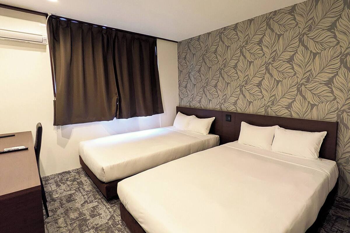 Habitación de hotel con dos camas, un escritorio y una ventana con cortinas.