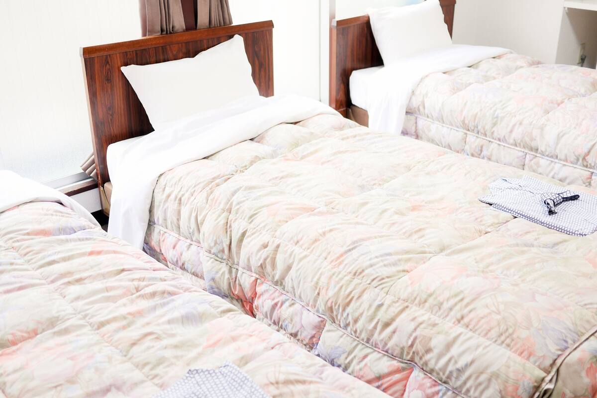 Habitación de hotel con tres camas individuales, cada una con cabecero de madera y ropa de cama estampada con motivos florales.