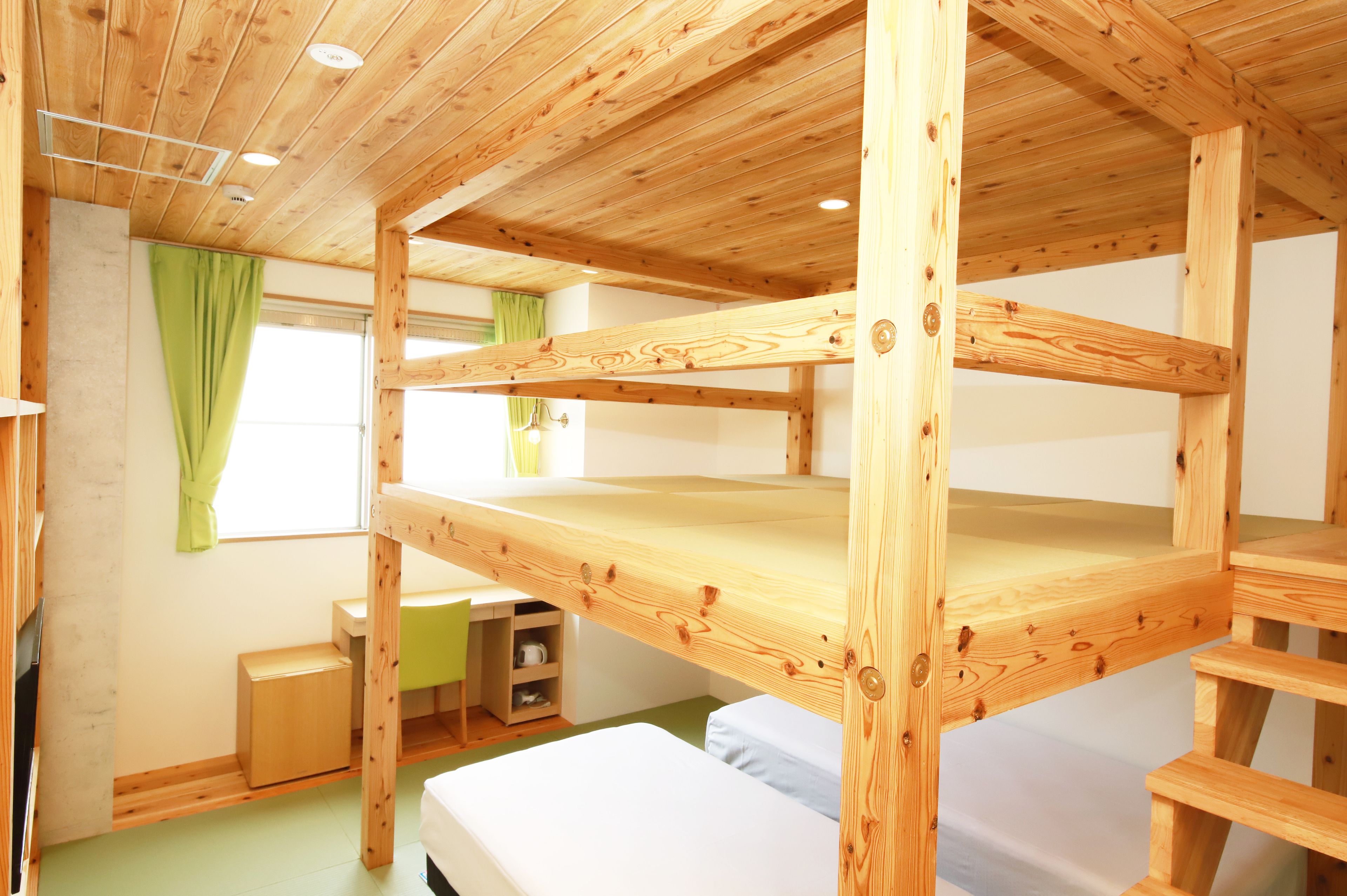 A bunk bed room with wooden beams, a desk, and a small cabinet.