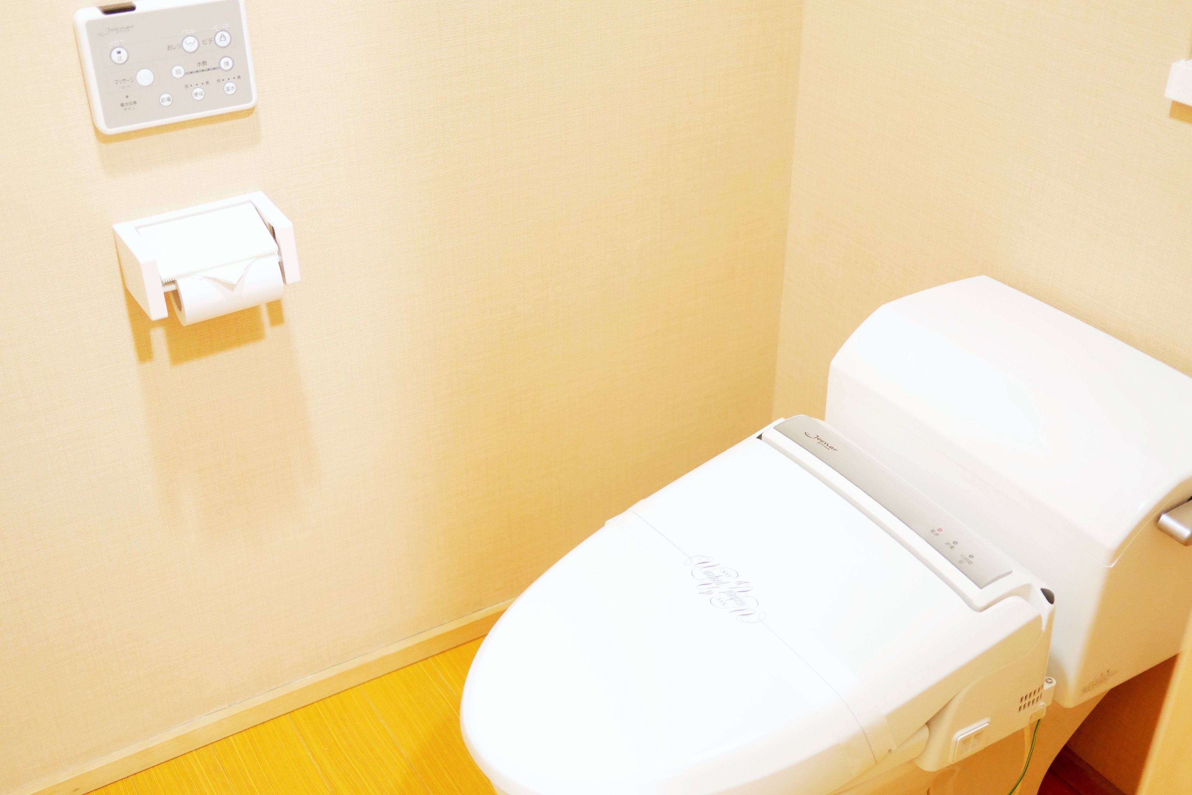 A white toilet with a control panel and a paper towel dispenser on the wall.