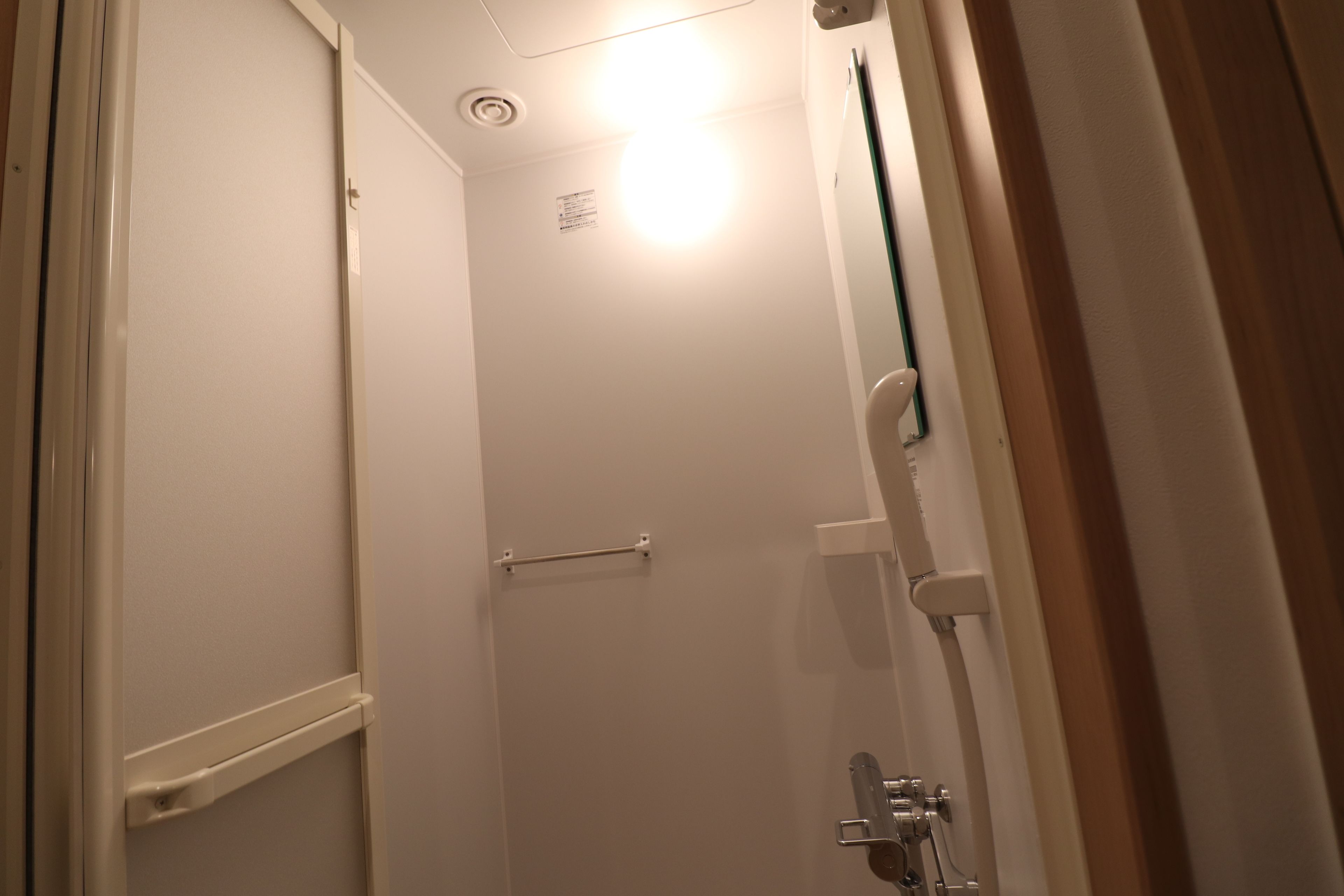 Un baño estrecho con paredes blancas, zona de ducha, toallero y un dispensador de papel higiénico a la vista.