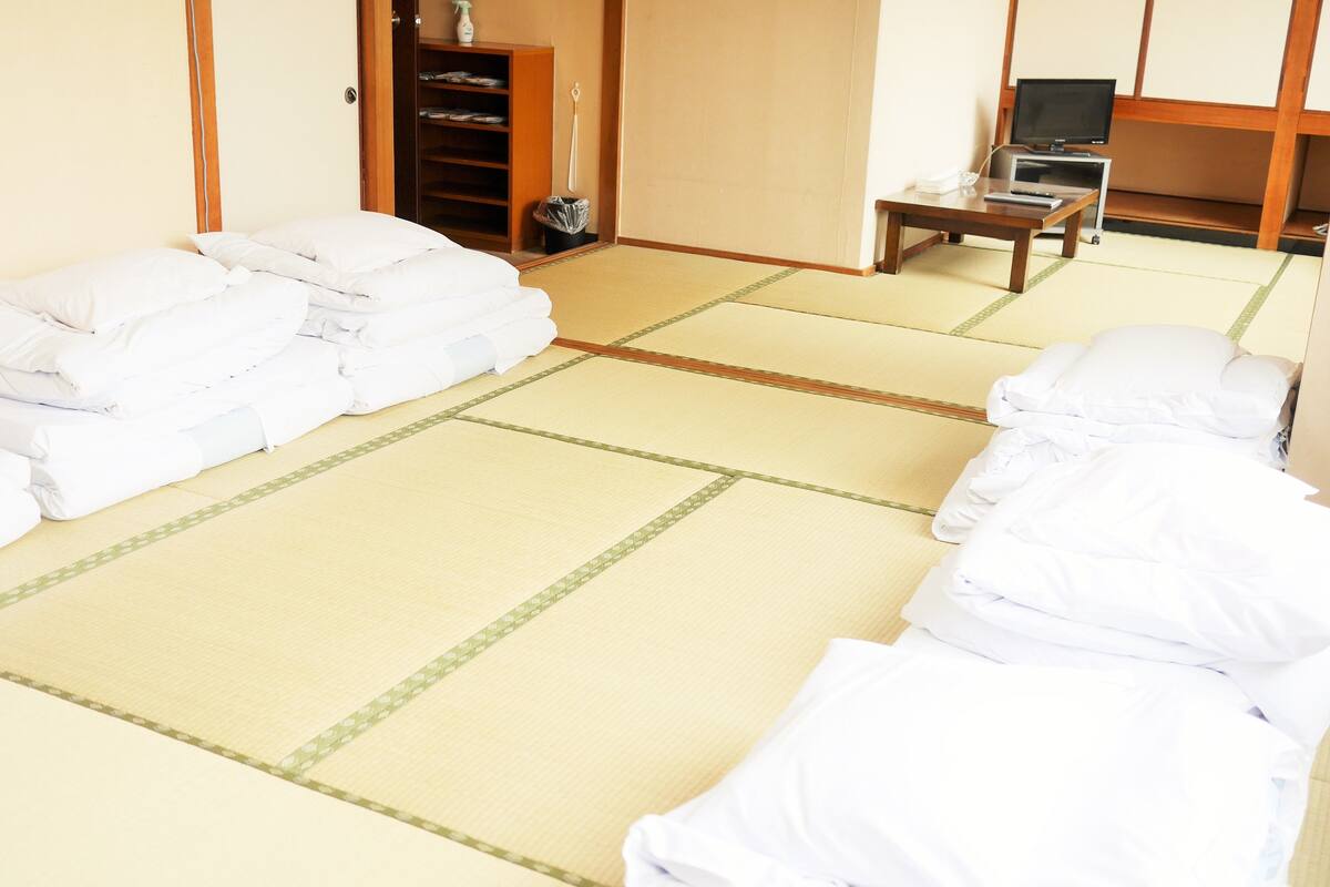 Una habitación japonesa tradicional con suelo de tatami, un futón, una televisión y una pequeña mesa con un control remoto.