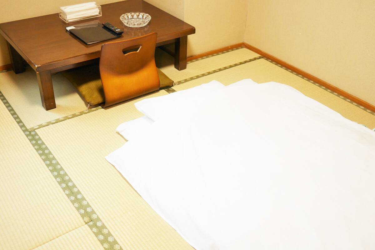 Una habitación con tatami, una mesa de madera, una silla y un felpudo blanco en el suelo.