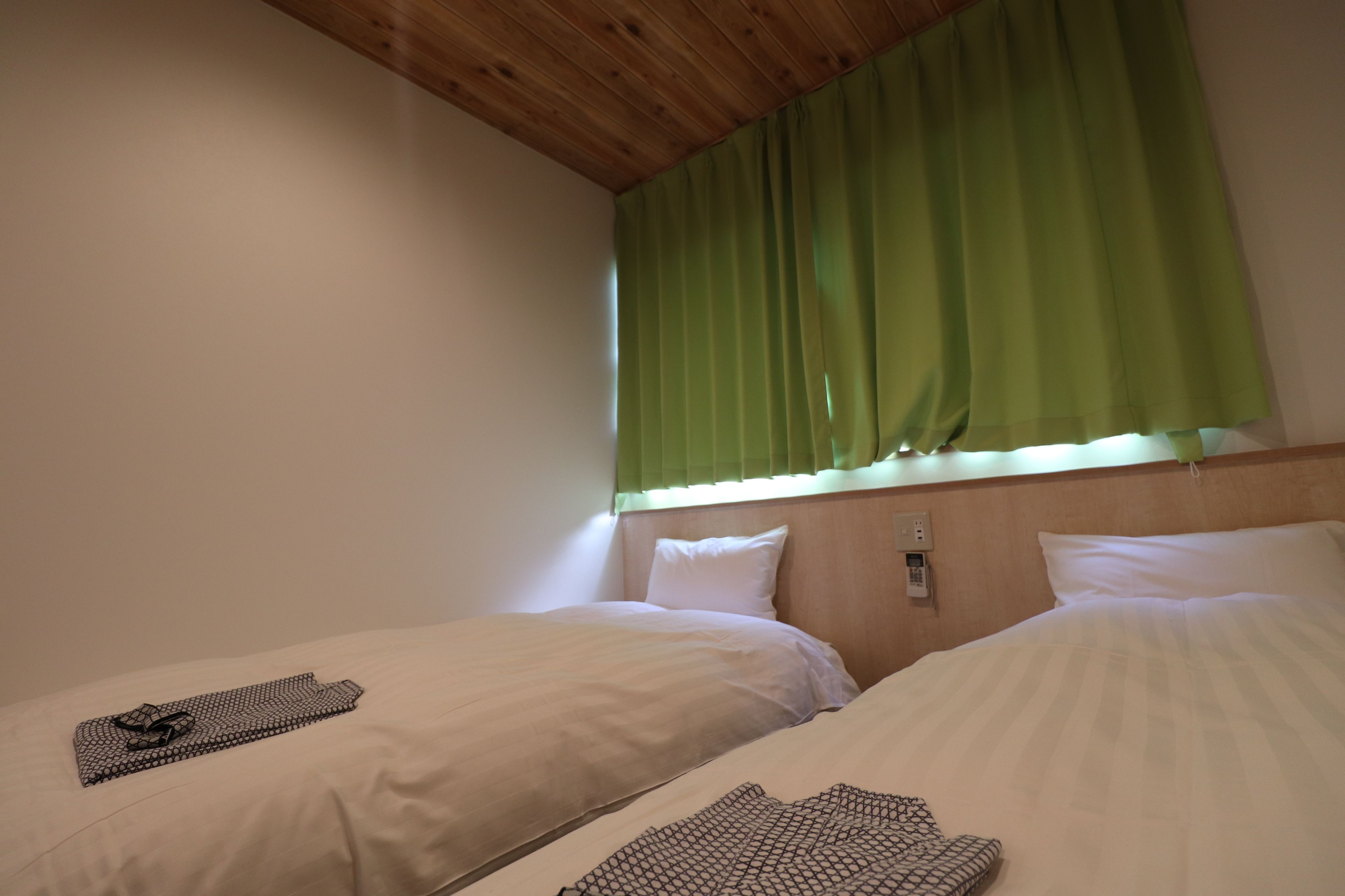 Een hotelkamer met twee bedden, een houten plafond en een raam met groene gordijnen.