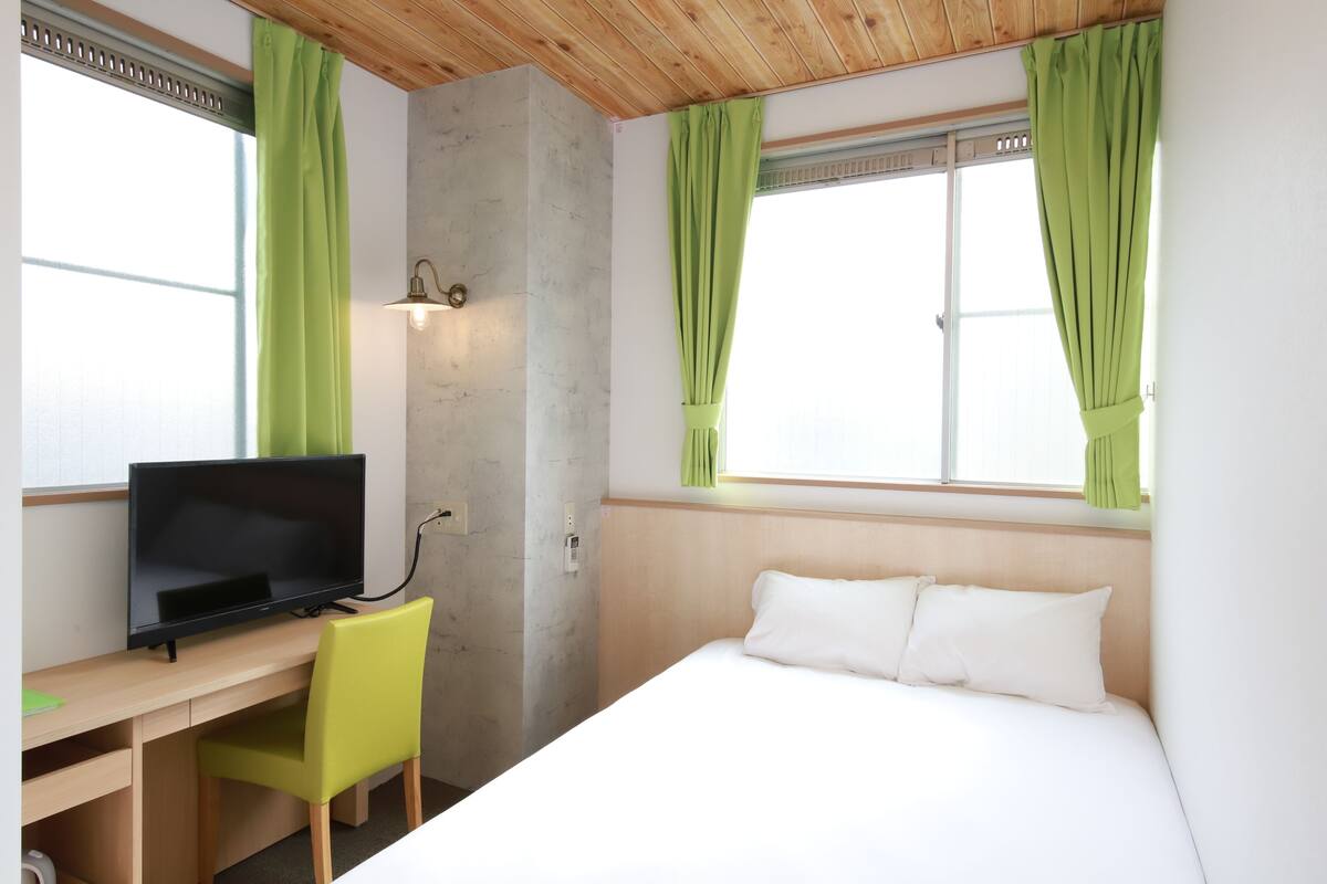 Una habitación de hotel con una cama, un escritorio con televisor y cortinas verdes.
