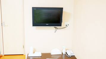 A room with a mounted television on the wall, a wooden table with a remote control, a telephone, and a spray bottle.