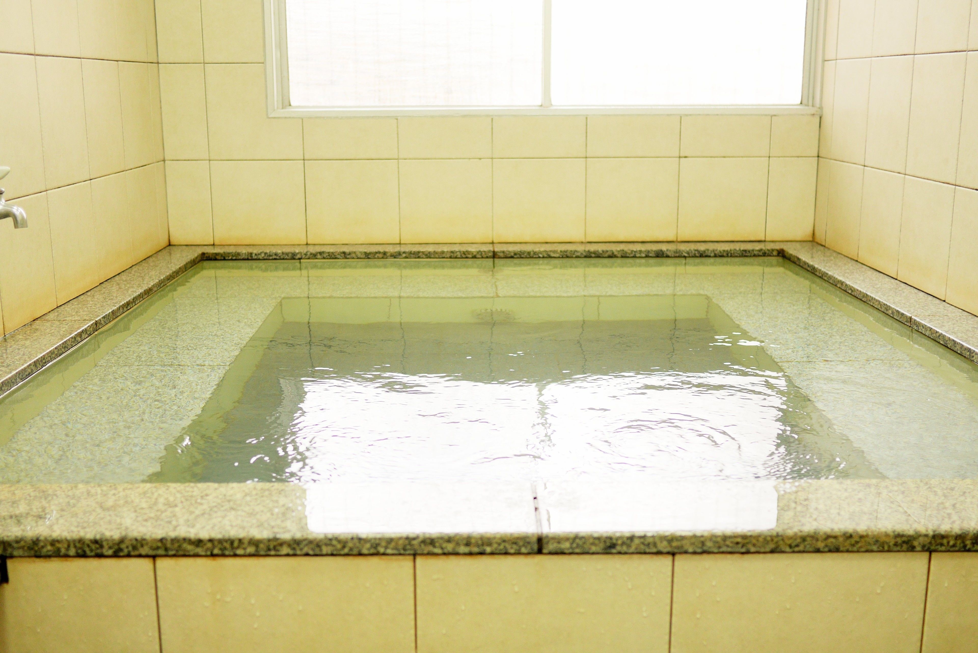 A rectangular hot tub with clear water, surrounded by yellow tiles and a window above.