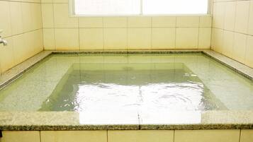 A rectangular hot tub with clear water, surrounded by yellow tiles and a window above.