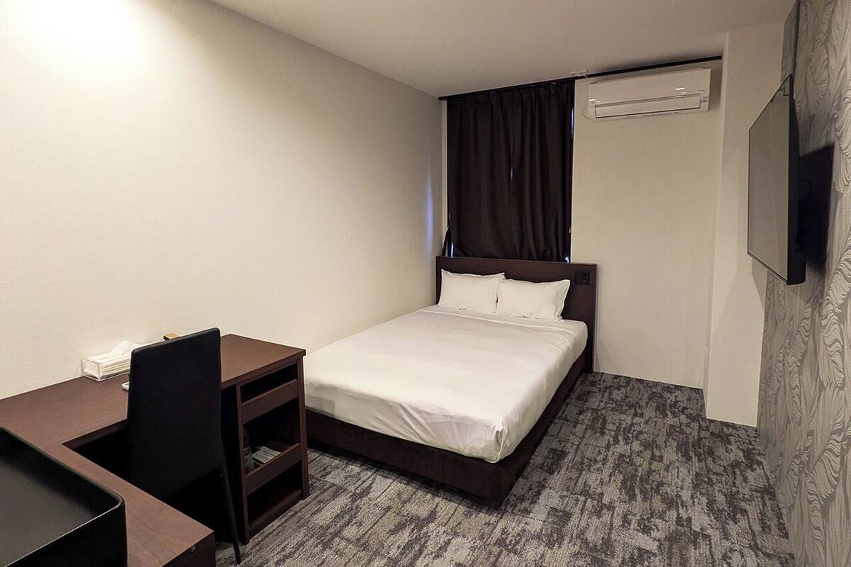 Una habitación de hotel pequeña con una cama individual, un escritorio, una silla y un televisor montado en la pared.