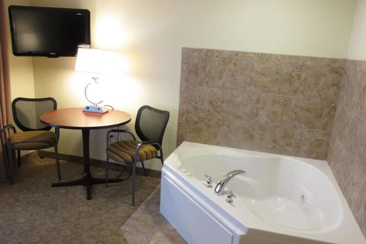 Une salle de bain avec une baignoire, une table avec des chaises, un téléviseur fixé au mur et un mur recouvert de carreaux.
