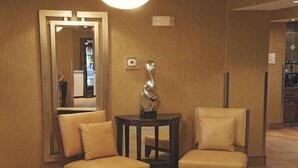 A lobby area with two leather armchairs, a small round table, and a mirror reflecting a vending machine. - La Quinta Inn & Suites by Wyndham Bismarck (Bismarck)