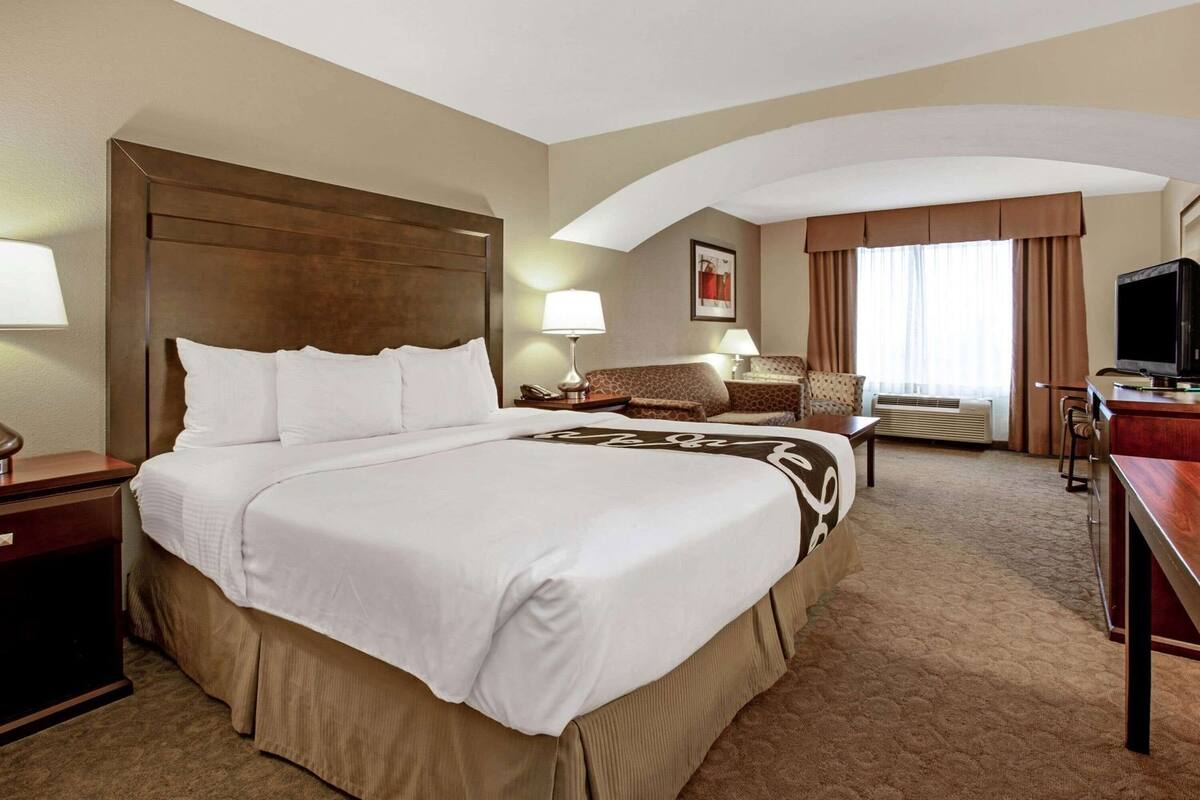 Une chambre d’hôtel avec un grand lit, un bureau, une chaise, une télévision et une fenêtre avec des rideaux.