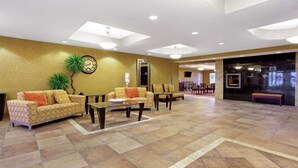 A spacious lobby with a high ceiling, patterned sofas, a coffee table, and a large clock on the wall. - La Quinta Inn & Suites by Wyndham Bismarck (Bismarck)