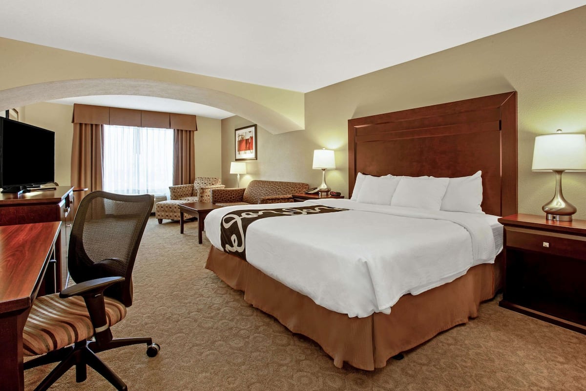 Une chambre d’hôtel avec un grand lit, un bureau avec une chaise, une télévision et une fenêtre avec des rideaux.