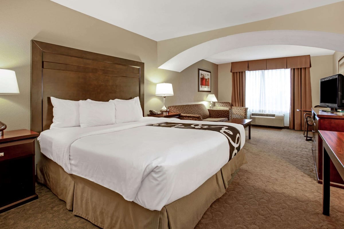 Une chambre d’hôtel avec un grand lit, un bureau, une chaise, une télévision et une fenêtre avec des rideaux.