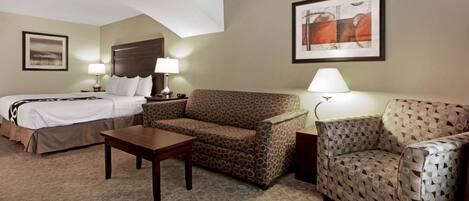 A hotel room with a bed, a sofa, a small table, and two lamps.