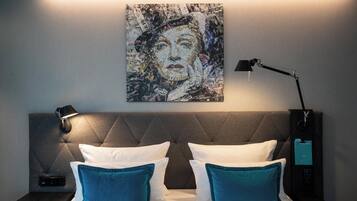 A hotel room with a tufted headboard, a bedside table with a lamp, and a wall-mounted artwork.