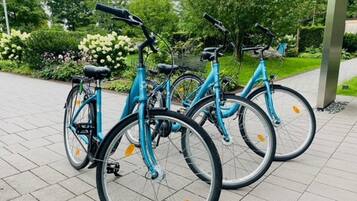 Una hilera de bicicletas azules estacionadas en un área pavimentada con un jardín al fondo.