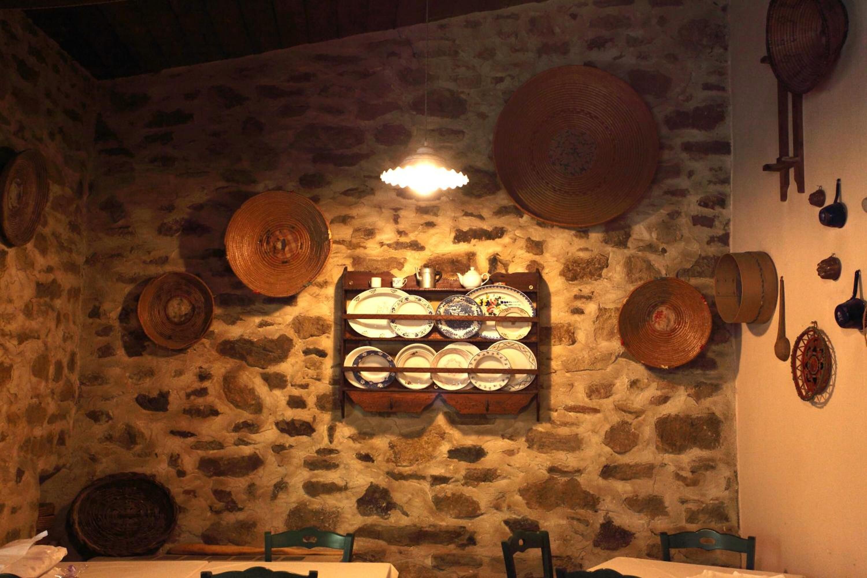 A rustic room with stone walls, a wooden shelf with plates, and woven baskets.