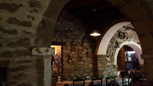 A stone-walled interior with arched ceilings, tables set for dining, and hanging light fixtures.