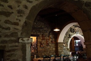 Un intérieur aux murs de pierre, avec des plafonds en arc de cercle, des tables dressées pour le repas et des luminaires suspendus.