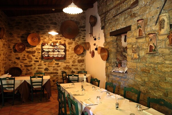 A rustic dining area with stone walls, wooden tables, and green chairs.