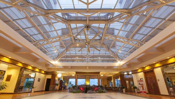 A spacious lobby with a high ceiling and a glass roof, featuring a central seating area with a decorative rock arrangement.