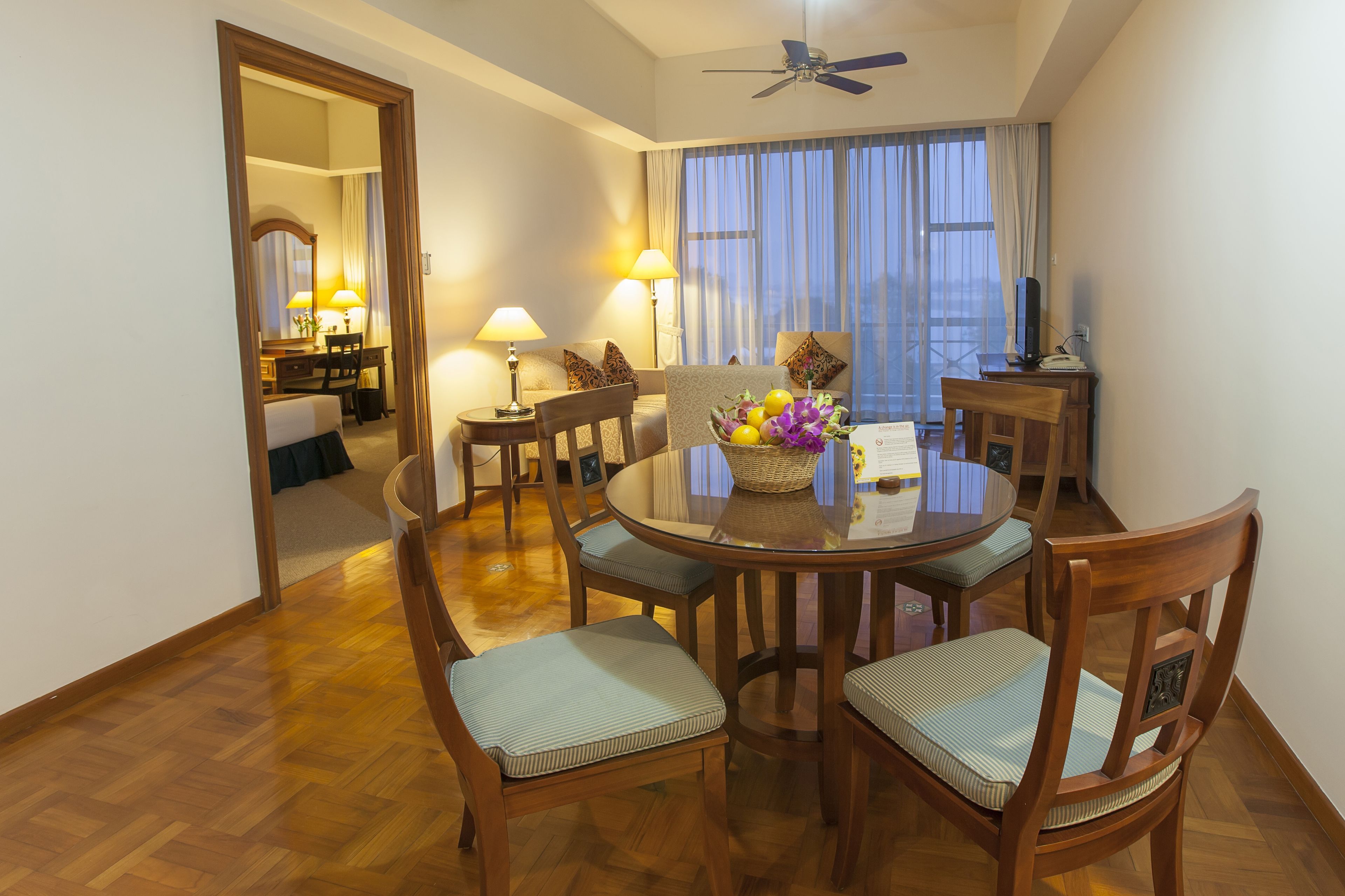 A hotel dining area with a round table, six chairs, and a ceiling fan.