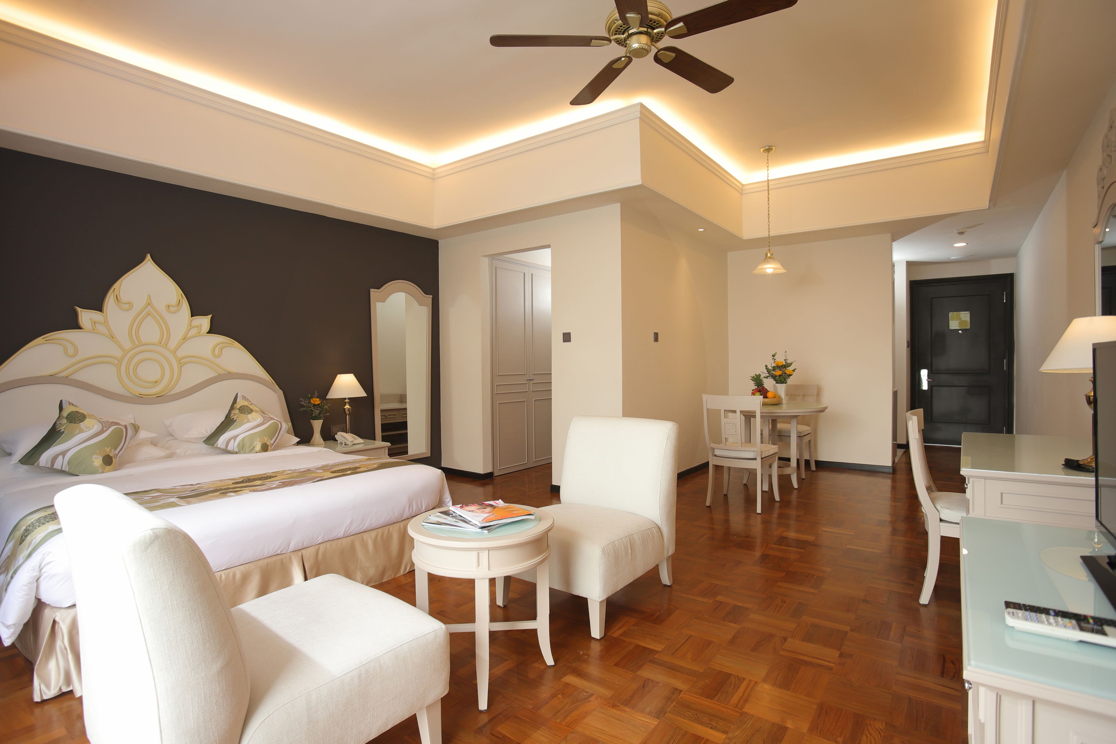 Une chambre d’hôtel comprenant un lit, un coin salon avec une table et des chaises, un ventilateur de plafond et un téléviseur.