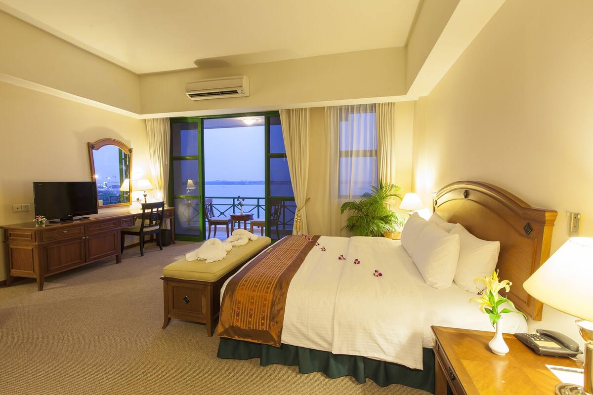 Een hotelkamer met een bed, bureau, televisie en uitzicht op zee.