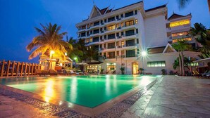 A hotel with a swimming pool, palm trees, and a well-lit facade.